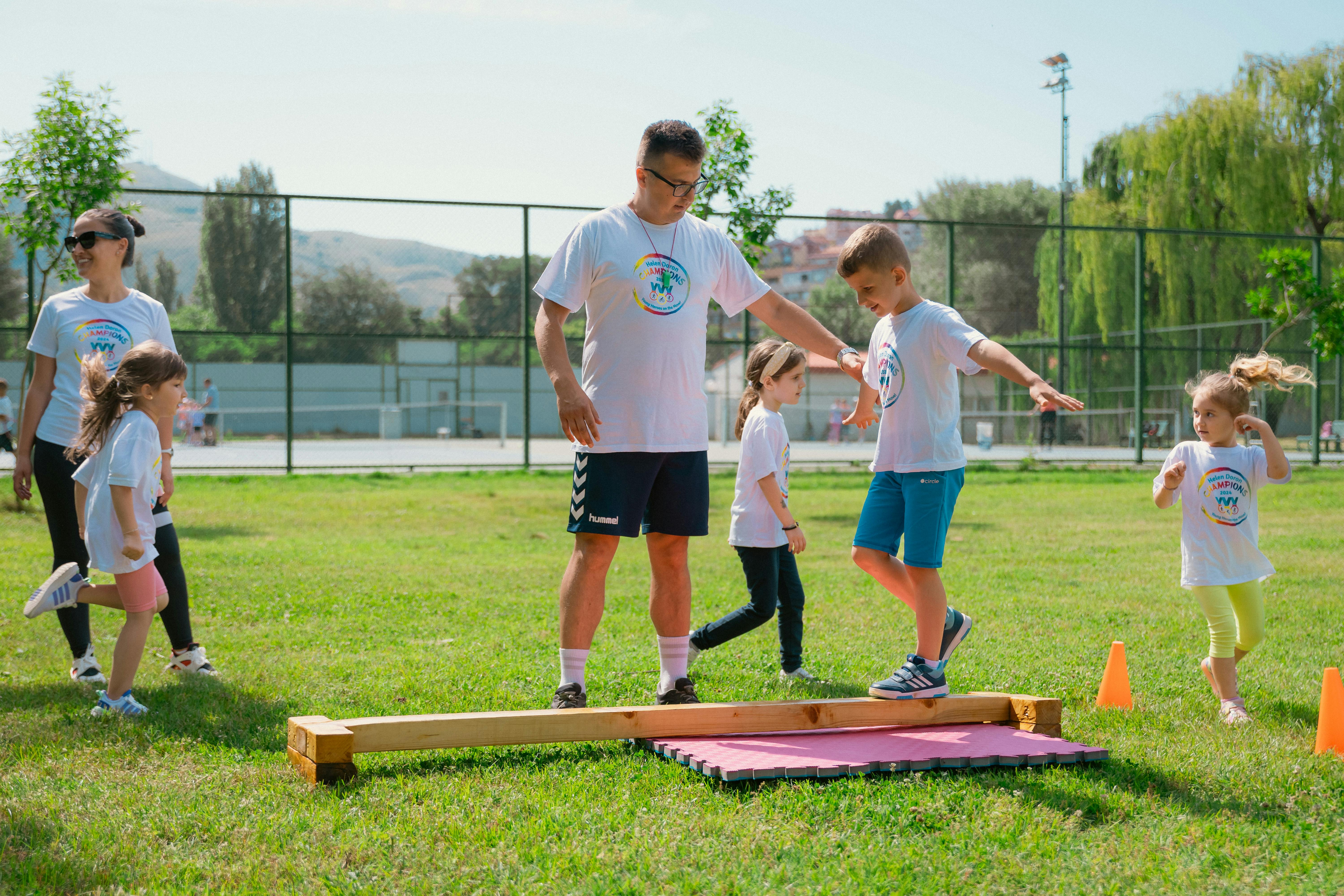 Camp instructor guiding a child on a wooden balance beam during outdoor games